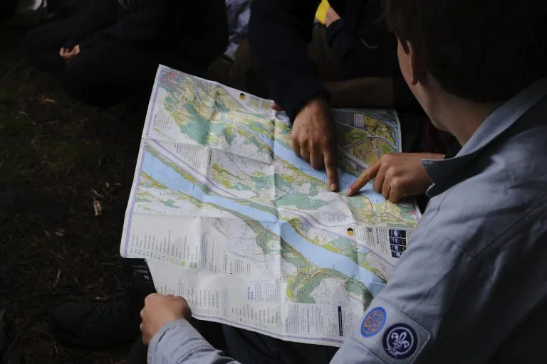 Pfadfinder in Kluft zeigen mit den Fingern auf eine ausgebreitete Wanderkarte